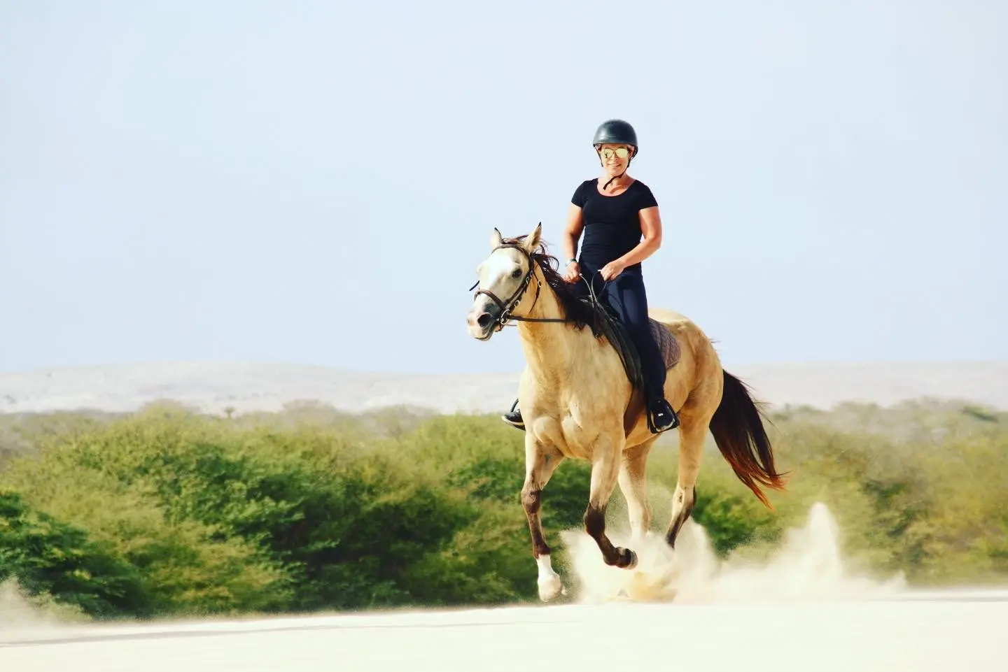 Smiling rider on a palomino horse in the dunes